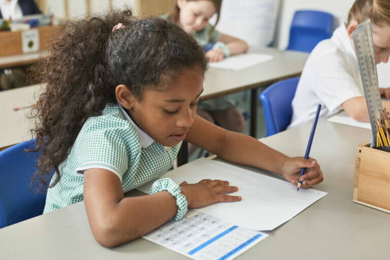 A happy young girl sitting at a school desk, surrounded by essential school supplies, highlighting the benefits of the United Way School Supply Drive for students in need.