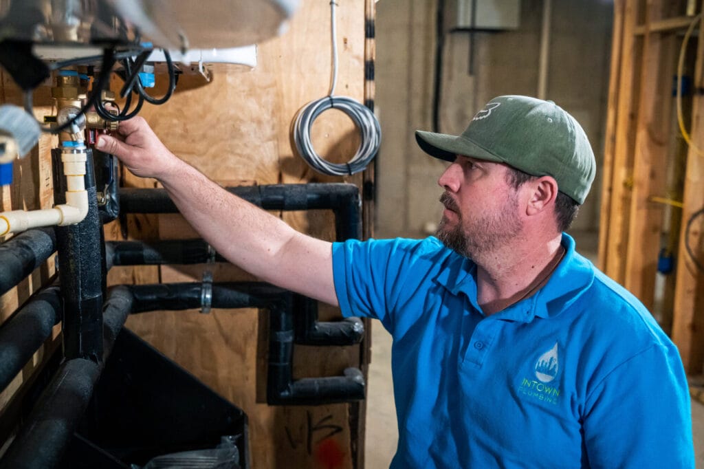An Intown Plumbing technician adjusting plumbing valves and connections on a water heater system to check for hard water sediment issues