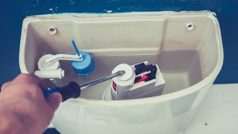 An image showing a person using a screwdriver to adjust the flushing mechanism inside an open toilet tank, illustrating the process of troubleshooting a running toilet.