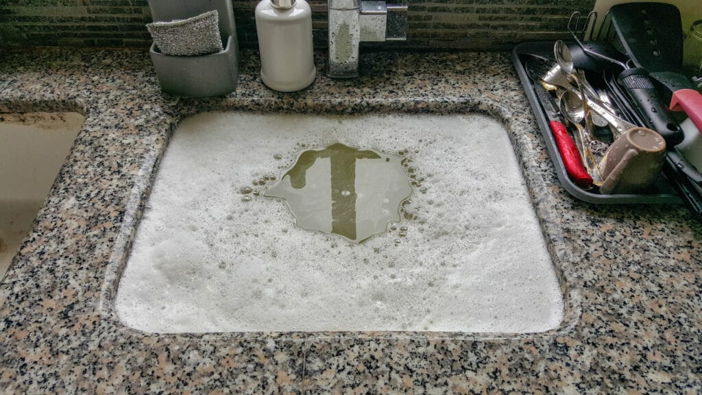 Kitchen sink with soapy water backing up due to a clog.