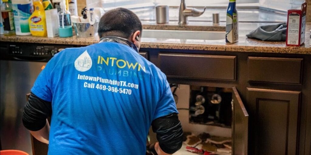 An Intown Plumbing technician wearing a blue company shirt works on a kitchen sink repair in a North Texas home.
