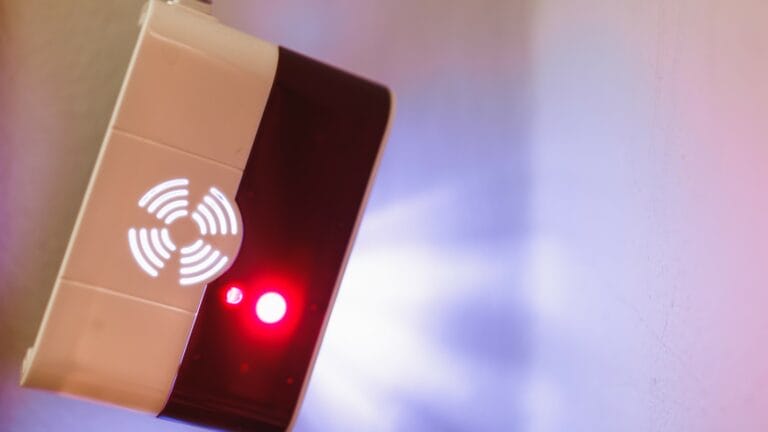A natural gas leak detector alarm mounted on a kitchen wall, with a glowing red alert light and a digital screen indicating high gas levels.