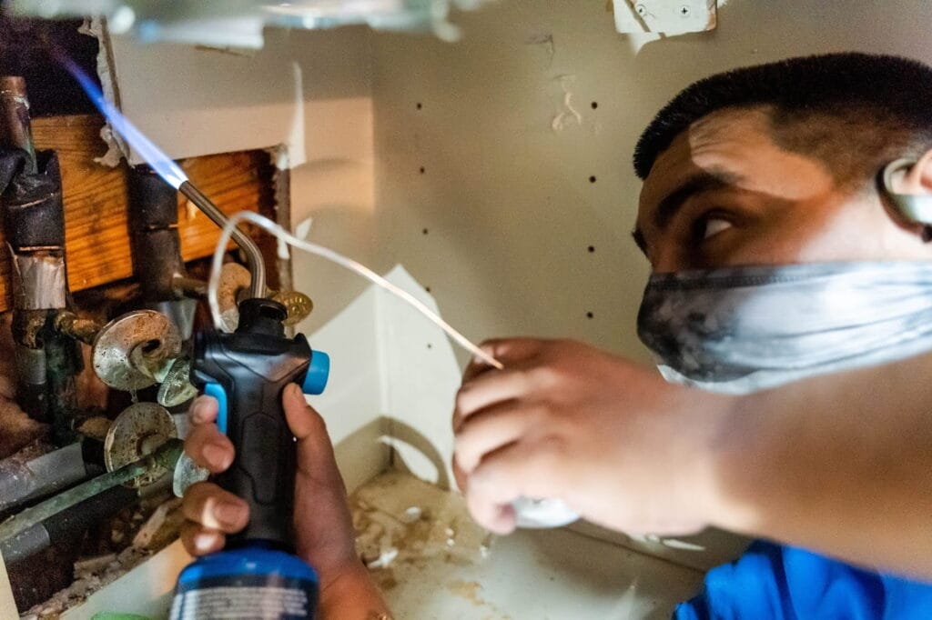 A professional plumber solders indoor pipes for homeowners researching what does a gas leak smell like in a house throughout the Dallas-Fort Worth area.