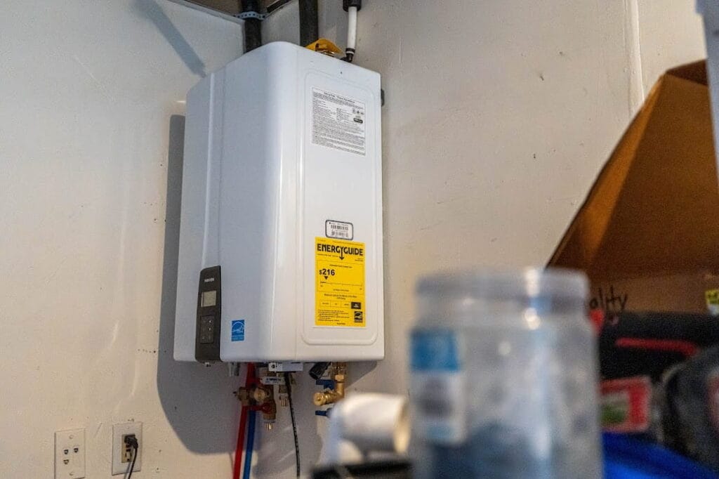 A Navien tankless water heater mounted on a white garage wall with visible plumbing connections and an EnergyGuide label.