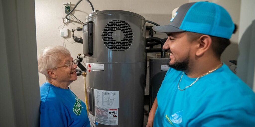An Intown Plumbing technician in a blue shirt and cap discusses a new energy-efficient water heater installation with a smiling homeowner.