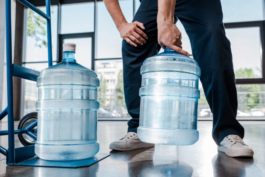 Cropped view of delivery man holding heavy bottle with water