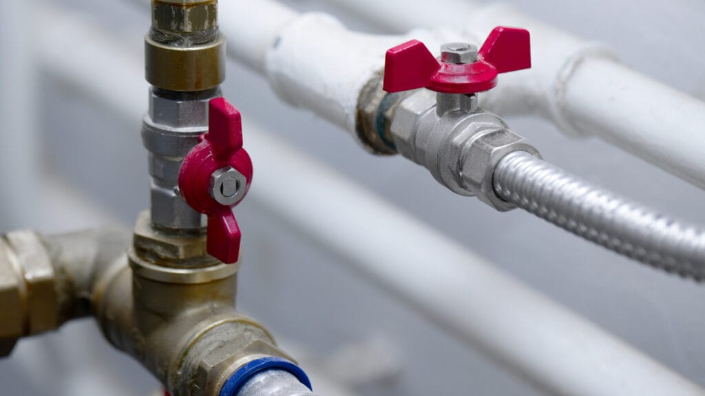 Close-up of a red valve on a home plumbing system, with connected metal pipes and flexible hose, illustrating components of residential plumbing.
