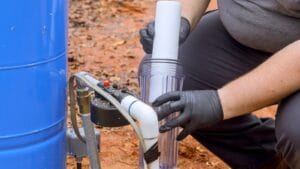 lose-up view of a person in gloves replacing a water filter cartridge to tackle hard water issues, demonstrating maintenance steps near a large blue storage tank outdoors.