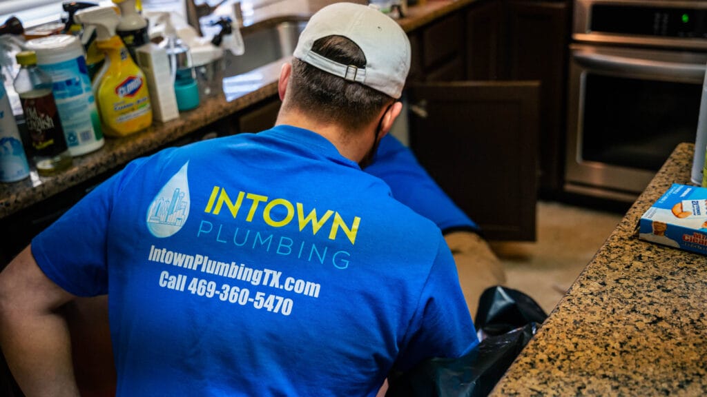 A plumber from Intown Plumbing working in a kitchen, highlighting professional help for unclogging garbage disposals.