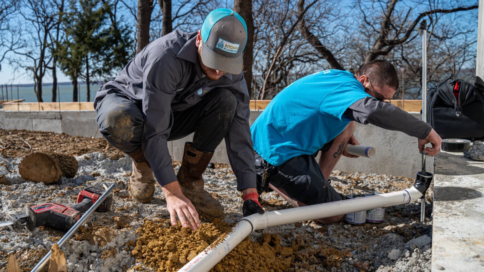 Two plumbers working outdoors on a sewer line installation, illustrating professional help for fixing clogged sewer lines.