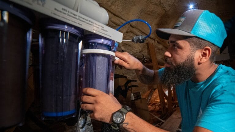 Technician inspecting a reverse osmosis water filtration system installed in an attic, ensuring proper setup and functionality.