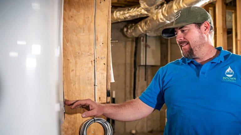A licensed plumber from Intown Plumbing adjusts a water heater inside a home basement, preparing to check the temperature settings.