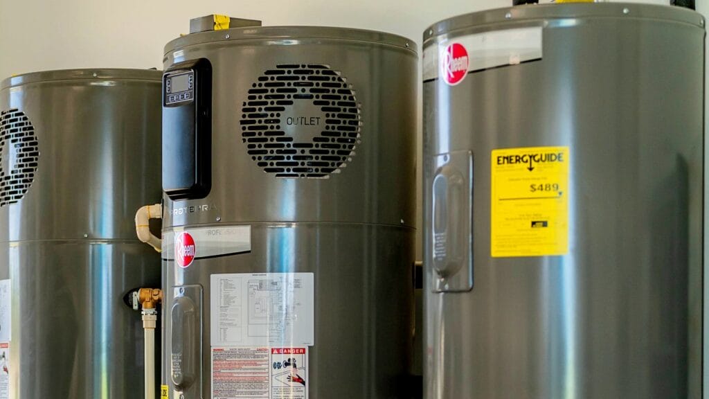 Three Rheem professional-grade water heaters installed side by side, including a ProTerra hybrid model with an energy guide label and outlet vent visible.