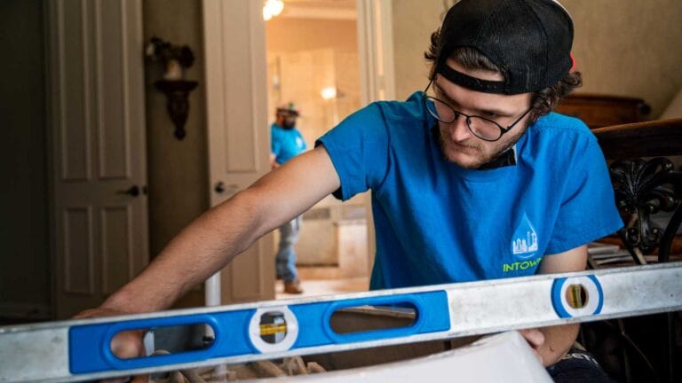 Intown Plumbing technician in a blue shirt using a spirit level to ensure precise and accurate installation of a white plumbing fixture in a bathroom.