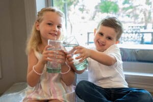 Two smiling children happily clinking glasses of clean tap water often make Dallas-Fort Worth parents wonder if a water filtration system is really worth the investment.