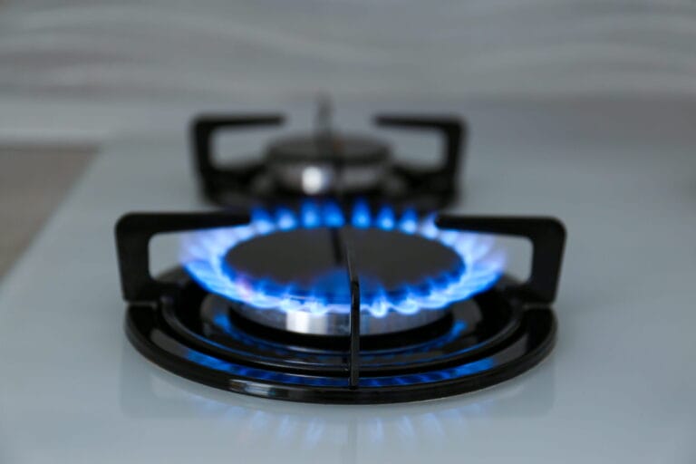 A close-up view of a kitchen gas stove burner ignited with a bright blue flame, highlighting the importance of proper gas line maintenance.