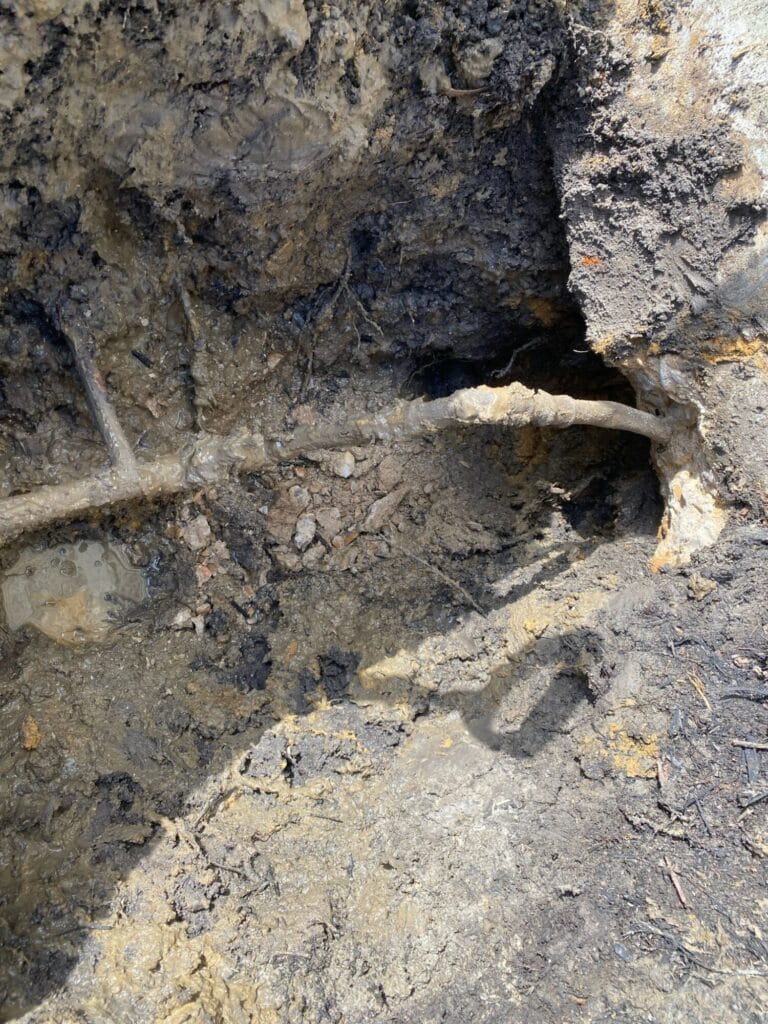 An excavated trench in Heath, Texas, revealing an underground water pipe with a visible leak in the soil.