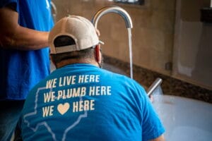 Two plumbers wearing blue shirts run a bathtub faucet to show how to test water line for leaks in Rockwall, TX.