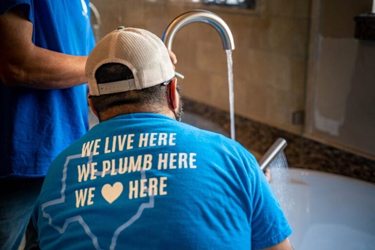 Two plumbers wearing blue shirts run a bathtub faucet to show how to test water line for leaks in Rockwall, TX.