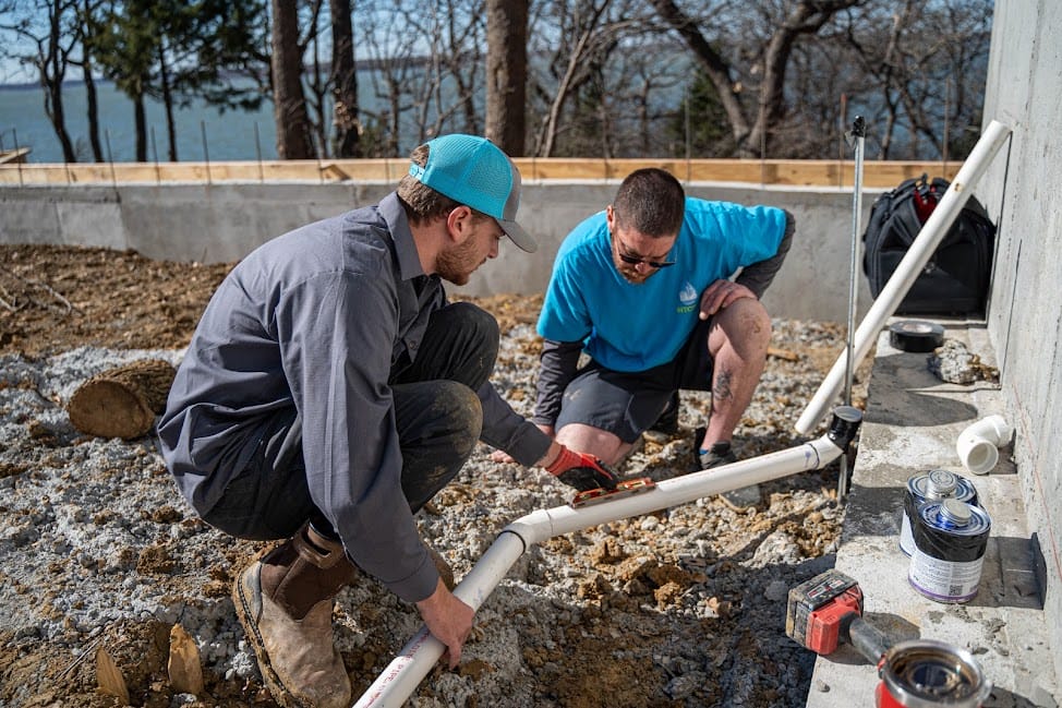 Two plumbing technicians use a level on an outdoor PVC pipe to demonstrate how to test water line for leaks in Rockwall, TX.
