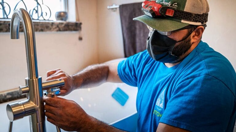 An Intown Plumbing technician wearing a headlamp and face mask carefully repairs a modern bathroom faucet.