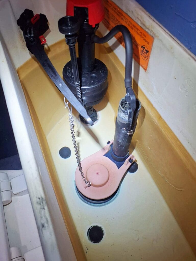The interior of a toilet tank showing the flush valve, fill valve, and a disconnected chain attached to the flush lever.