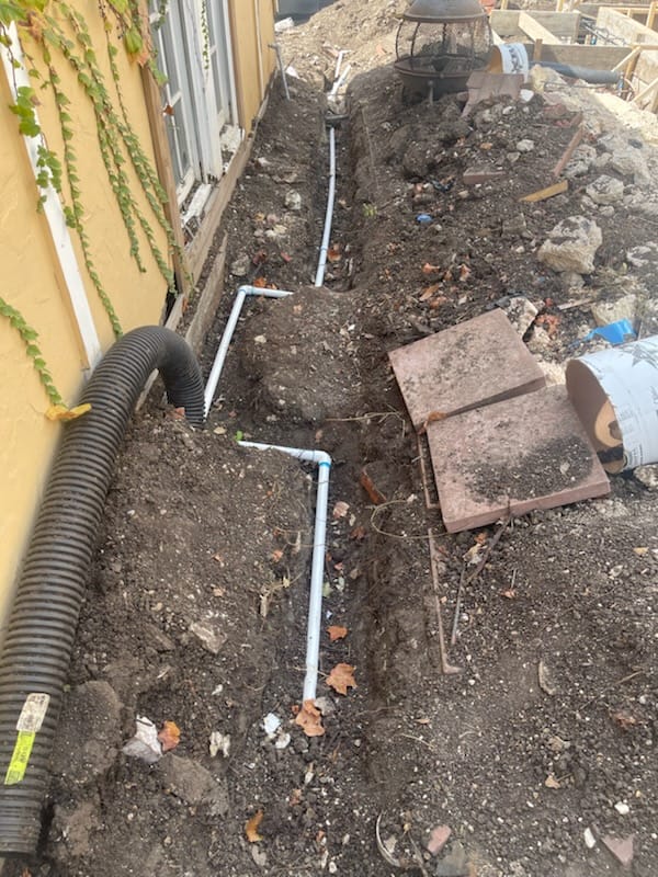 An open dirt trench excavated next to a residential home reveals exposed white PVC piping to visually demonstrate how to test water line for leaks in Rockwall, TX.