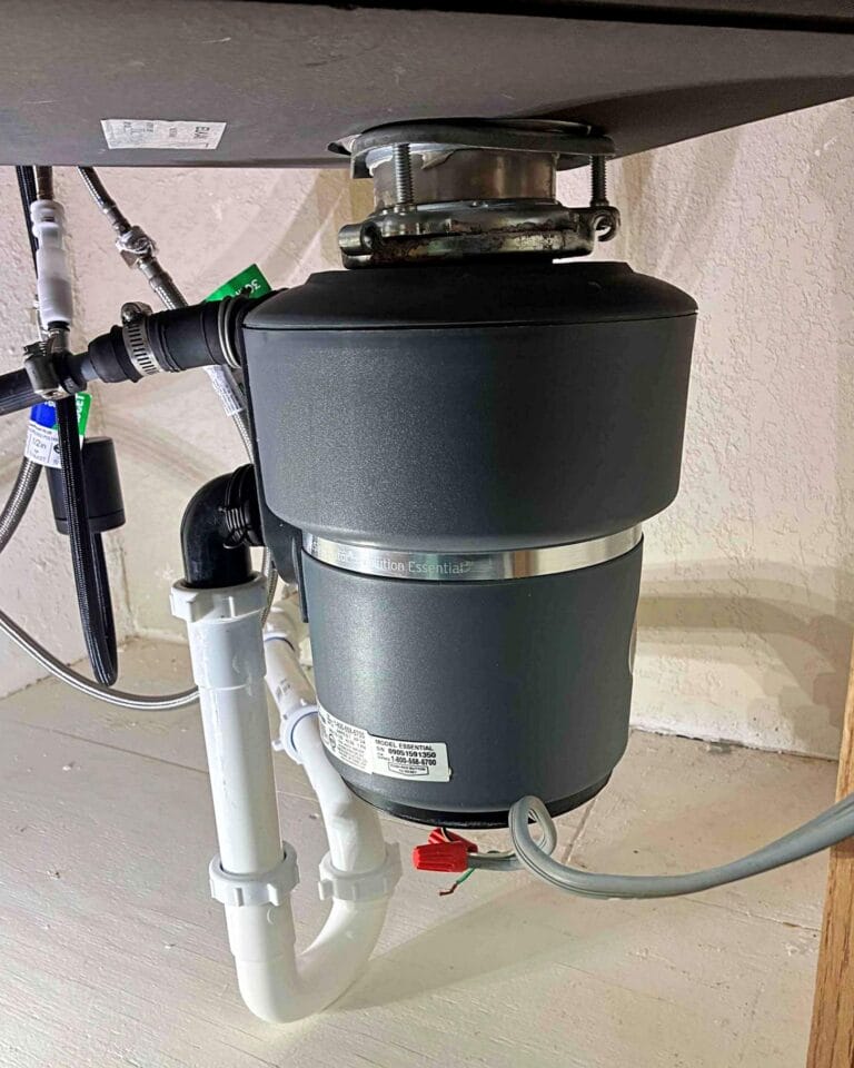 A newly installed InSinkErator garbage disposal unit mounted under a kitchen sink with connected plumbing and electrical wiring.