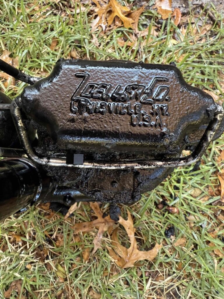 A close-up view of a black, heavy-duty sump pump unit with the manufacturer's name and Louisville, KY, U.S.A. branding visible on the casing, resting on grass during a replacement project in Royse City, Texas.