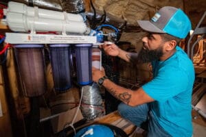 A technician from Intown Plumbing performs maintenance on a Bulk Reef Supply reverse osmosis water filtration system in an attic.