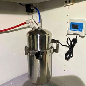 A stainless steel reverse osmosis water filtration system installed under a sink, featuring blue and red tubing connected to a DigiFlow 8100T water monitor.