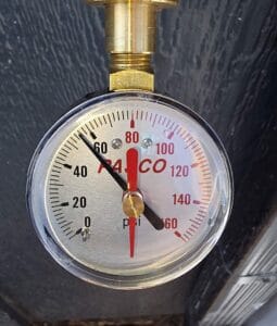 A close-up view of a circular analog pressure gauge showing a reading of approximately 55 PSI, used during a water service line inspection.