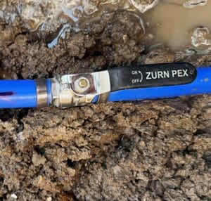 A Zurn Pex blue pipe ball valve installed in a muddy trench during a water meter tie-in project in Irving, Texas.