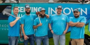Five professional plumbers from Intown Plumbing standing in front of their company van, with one holding a pipe wrench and another holding a plunger.