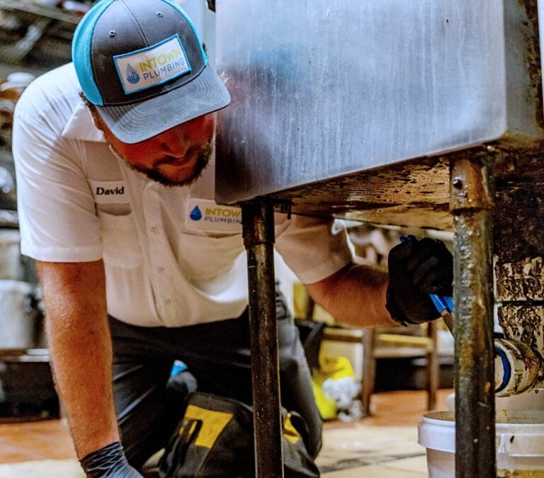 A plumber named David from Intown Plumbing wearing a branded hat and shirt performs a commercial plumbing repair on a sink drain.