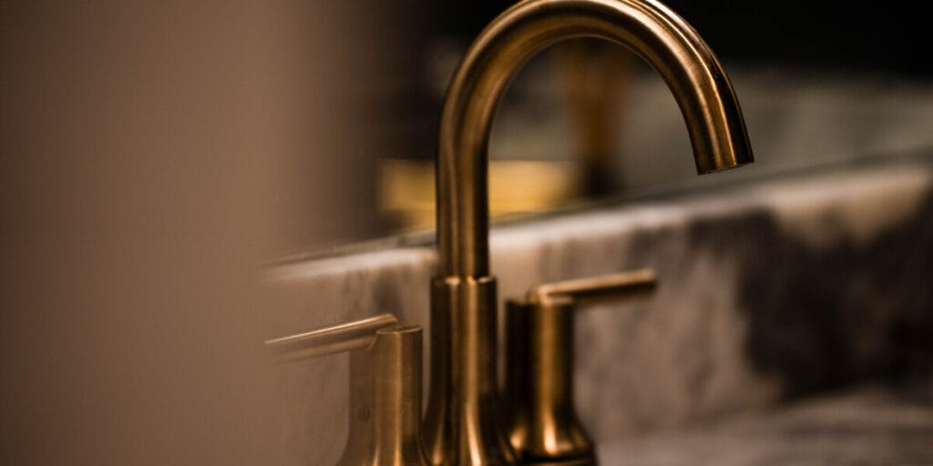 A close-up view of a modern, brushed brass bathroom faucet mounted on a marble countertop, reflecting the elegant design of a home plumbing installation.