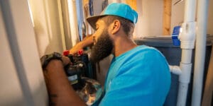 A plumber from Intown Plumbing wearing a blue shirt and cap works on installing a water softener system in a utility closet.