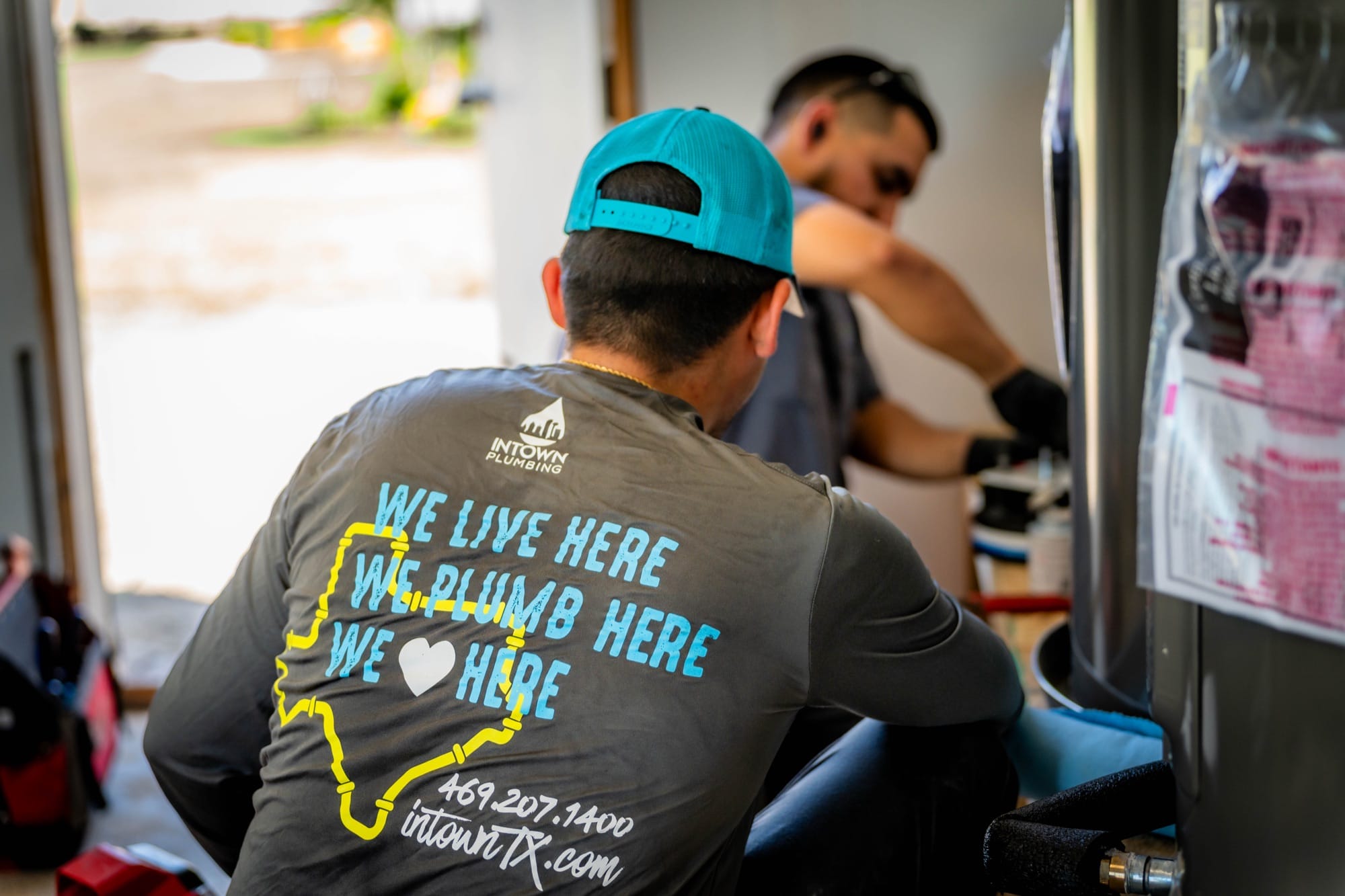 Intown Plumbing technician in a "We live here, we plumb here" shirt working on a water heater